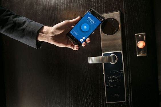 Mano sosteniendo un smartphone con tecnología en una aplicación para desbloquear una puerta de hotel.