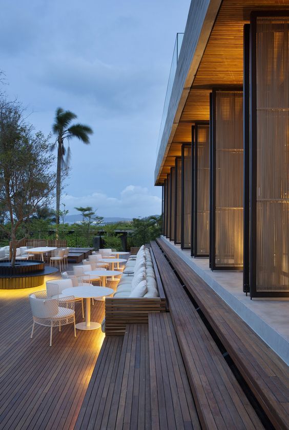 Terraza iluminada al anochecer, con mesas y sillas de diseño moderno y detalles en madera.