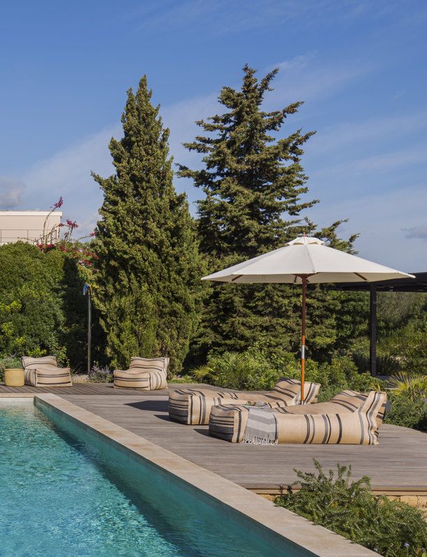 Área de piscina rodeada de vegetación con tumbonas de diseño casual y sombrilla blanca