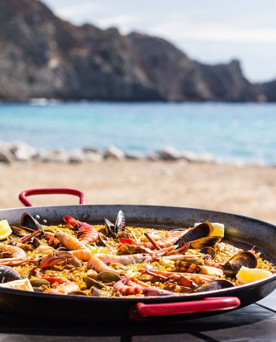 Paella de mariscos servida junto al mar con vistas a las olas.