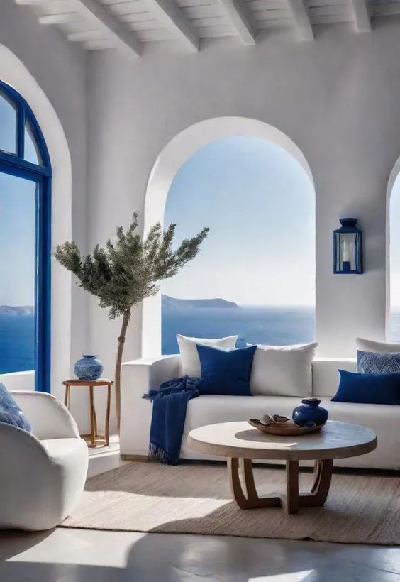 Sala de estar con ventanas arqueadas y vistas al mar, decorada en blanco y azul.