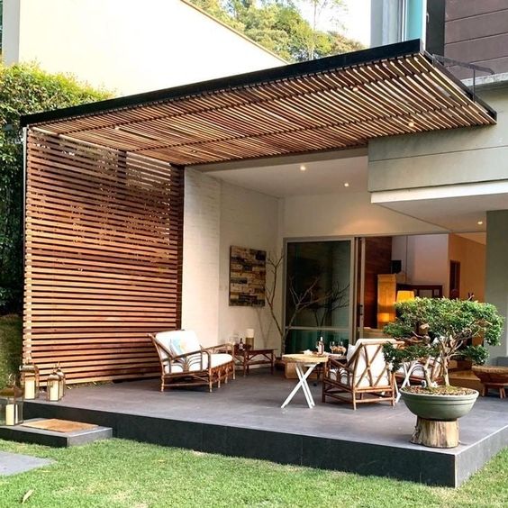 Porche cubierto con diseño de madera, muebles de exterior rústicos y un jardín al fondo.