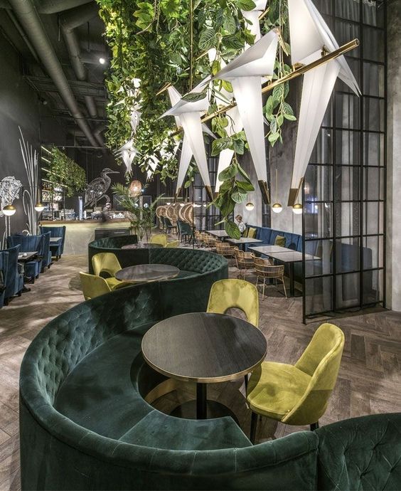 Restaurante con decoración vegetal suspendida y sofás en terciopelo verde.