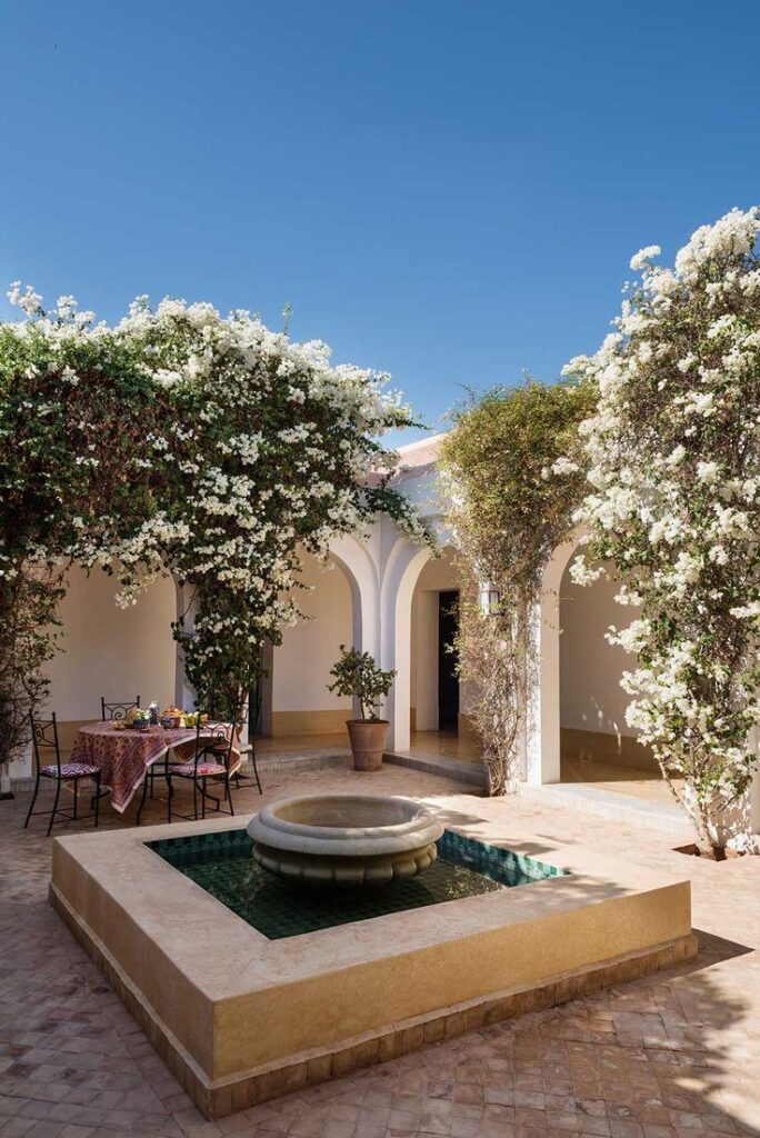 Jardín interior con fuentes, flores blancas y arquitectura mediterránea.