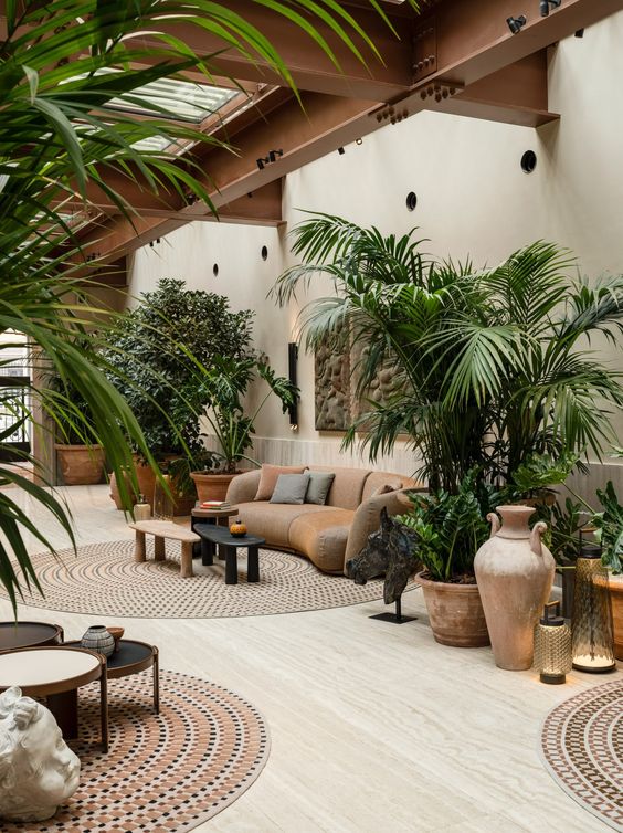 Espacio interior decorado con plantas tropicales, muebles de mimbre y cerámicas de gran formato.